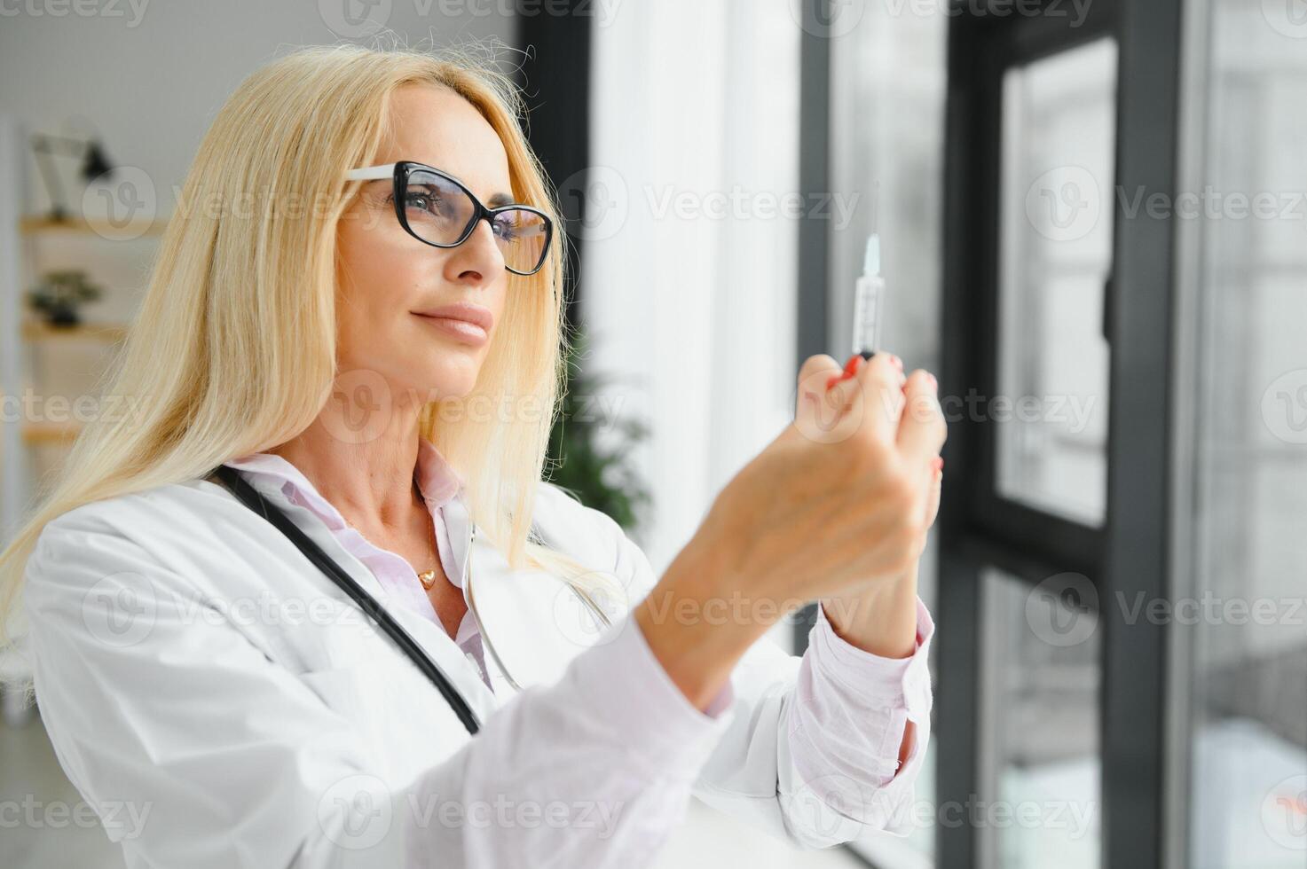 Portrait of middle age female doctor is wearing a white doctor's coat with a stethoscope around her neck. Smiling physician standing at private clinic photo