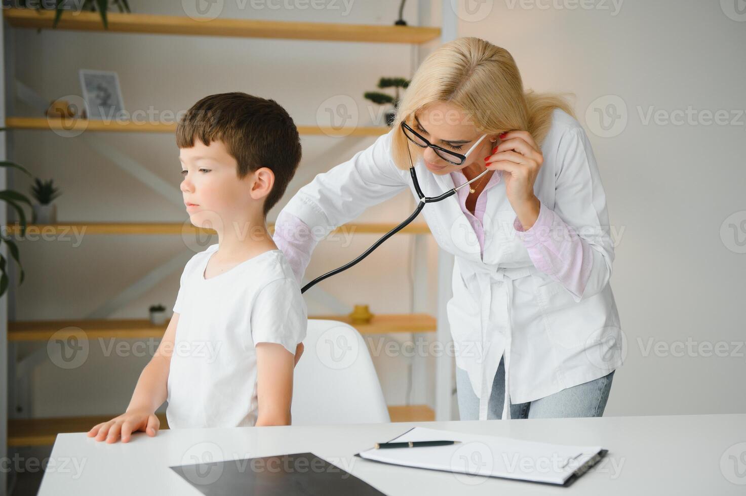 Doctor pediatrician examines child. Female doctor puts a stethoscope to a child's chest and listens to the little boy's heartbeat and lungs. Concept of health care and pediatric medical examination. photo