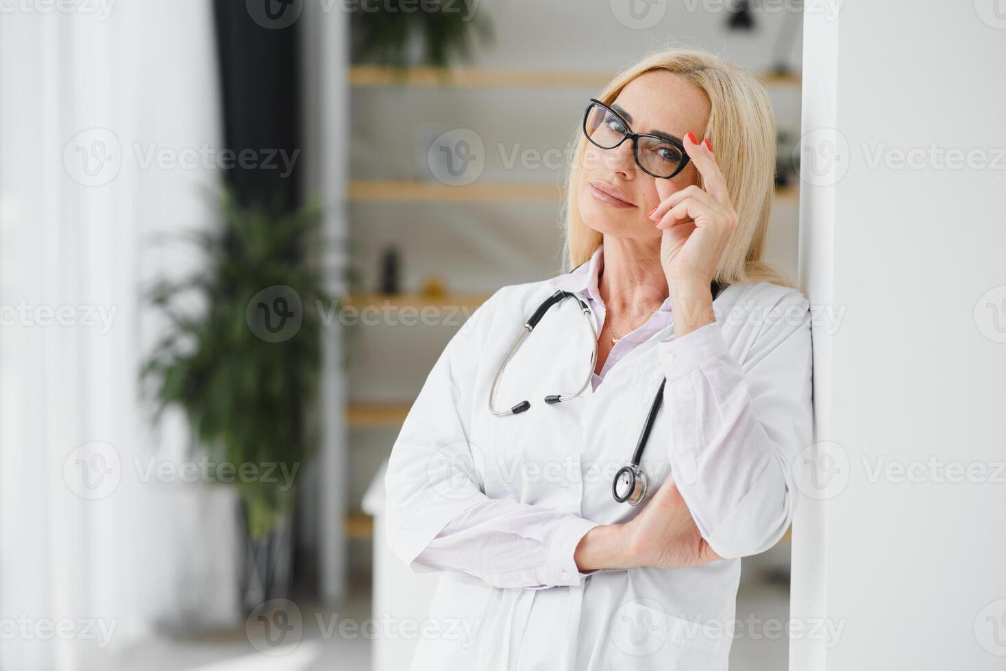 Portrait of middle age female doctor is wearing a white doctor's coat with a stethoscope around her neck. Smiling physician standing at private clinic photo