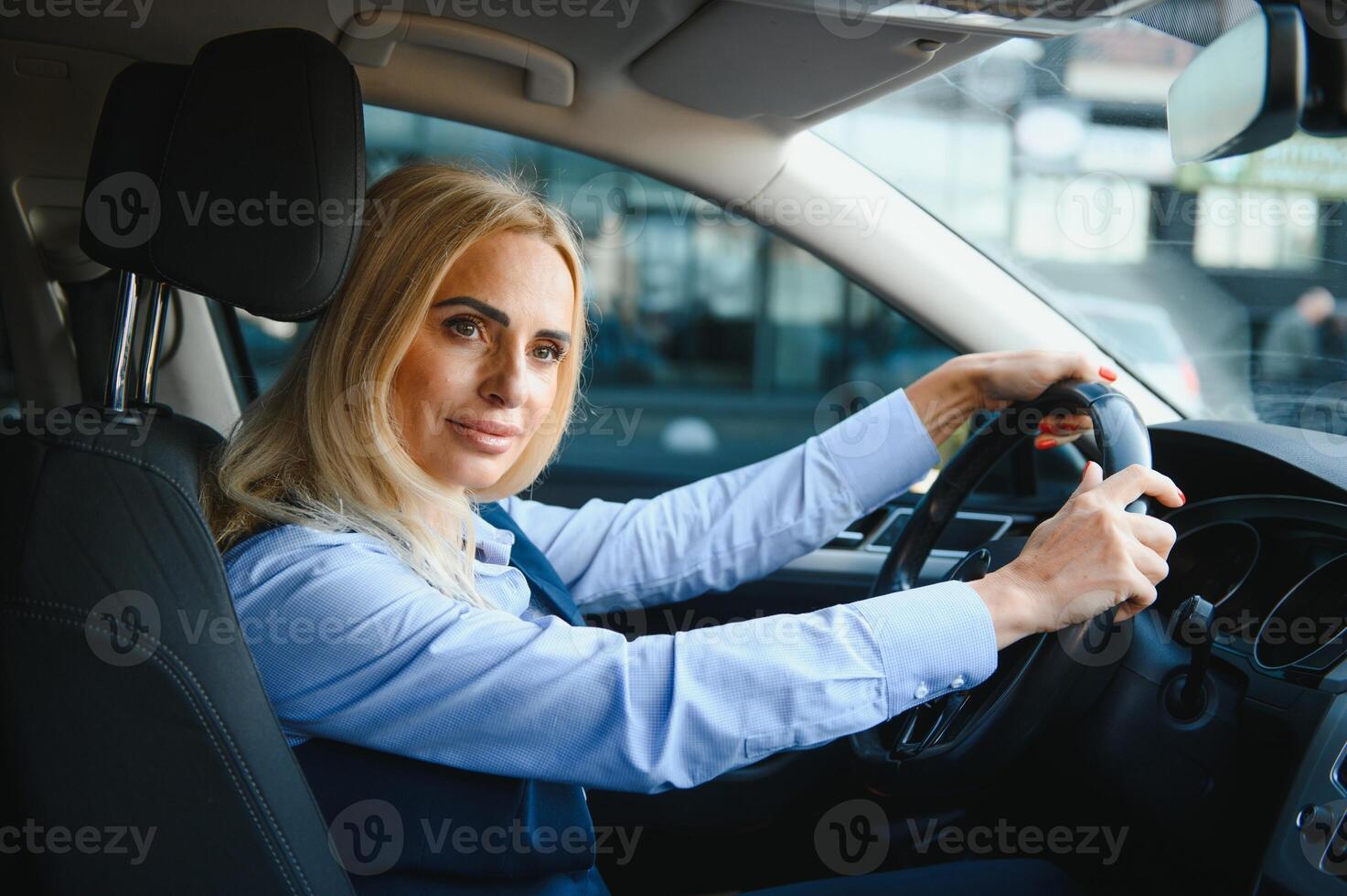 Portrait of a beautiful mature business woman driving a car, sitting behind steering wheel, looking at camera and smiling photo