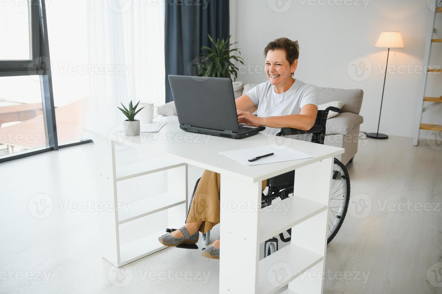 Freelancer in wheelchair using laptop near notebook and papers on table photo
