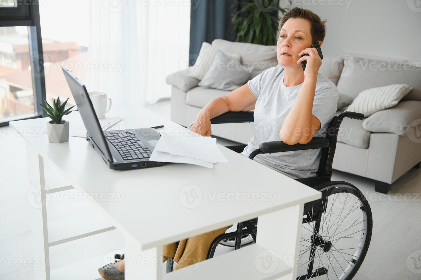 Middle age woman using laptop sitting on wheelchair at home photo