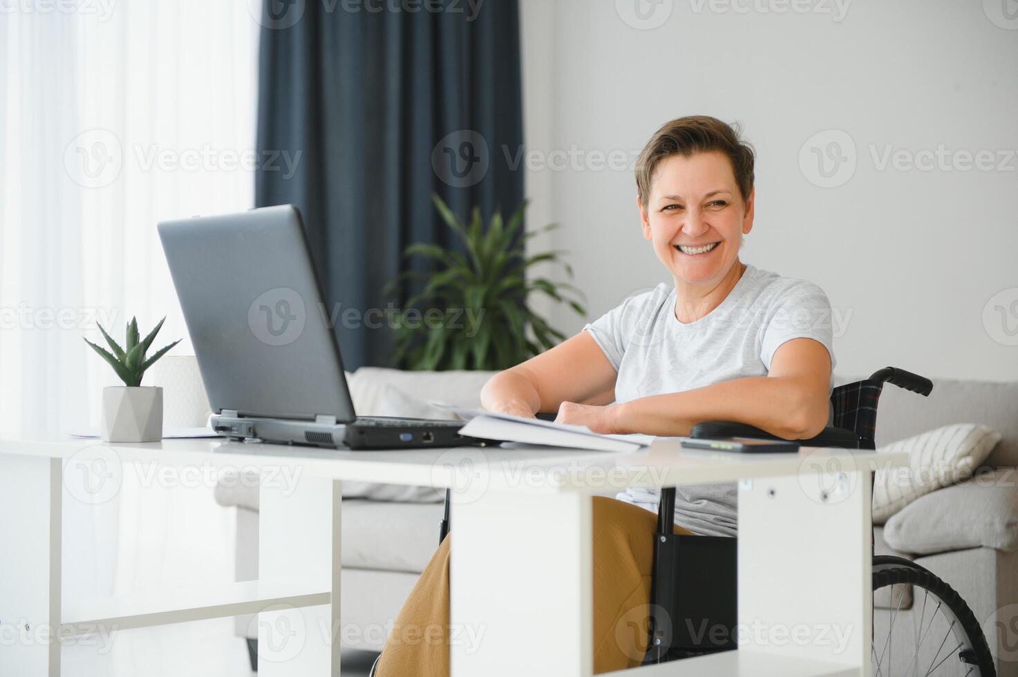Freelancer in wheelchair using laptop near notebook and papers on table photo