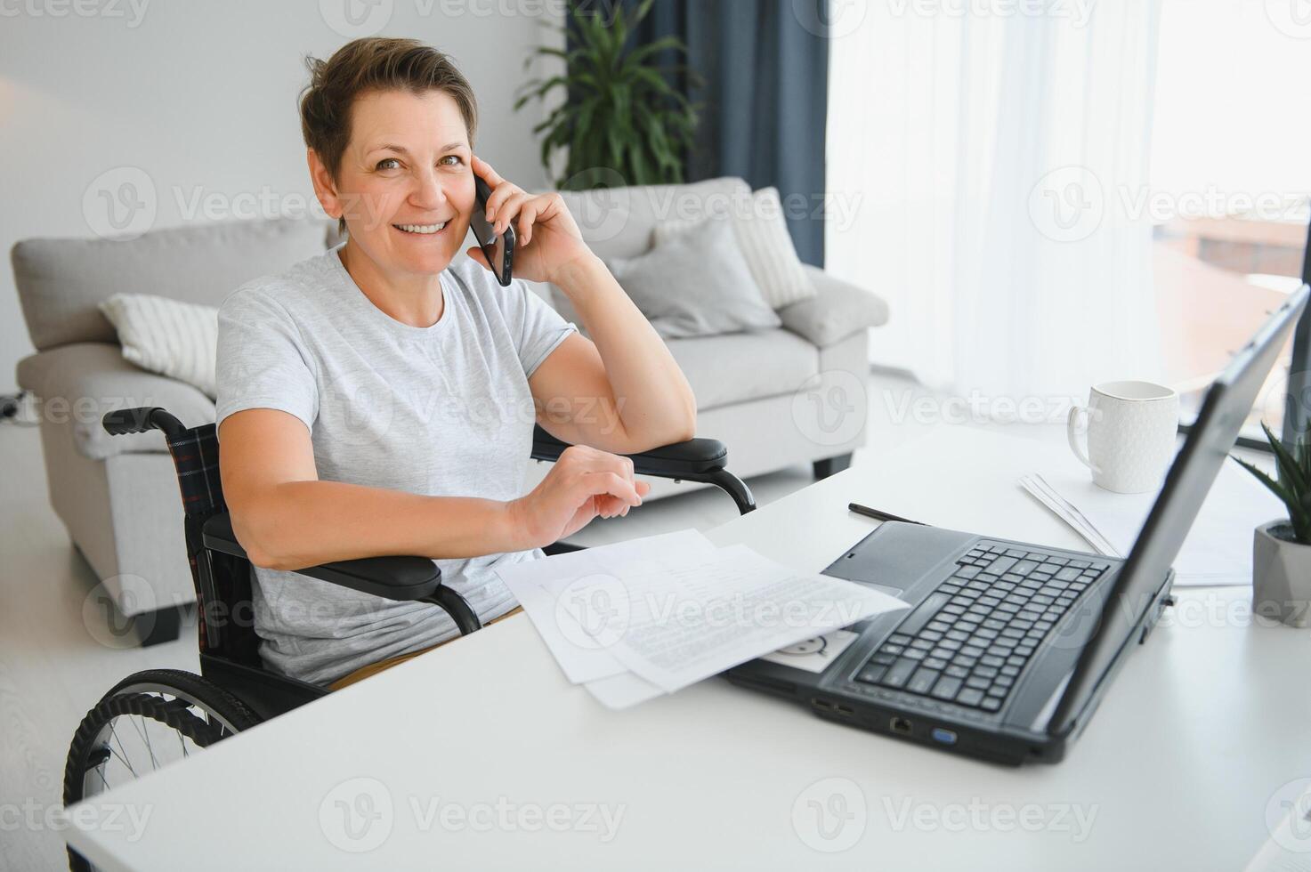 Middle age woman using laptop sitting on wheelchair at home photo