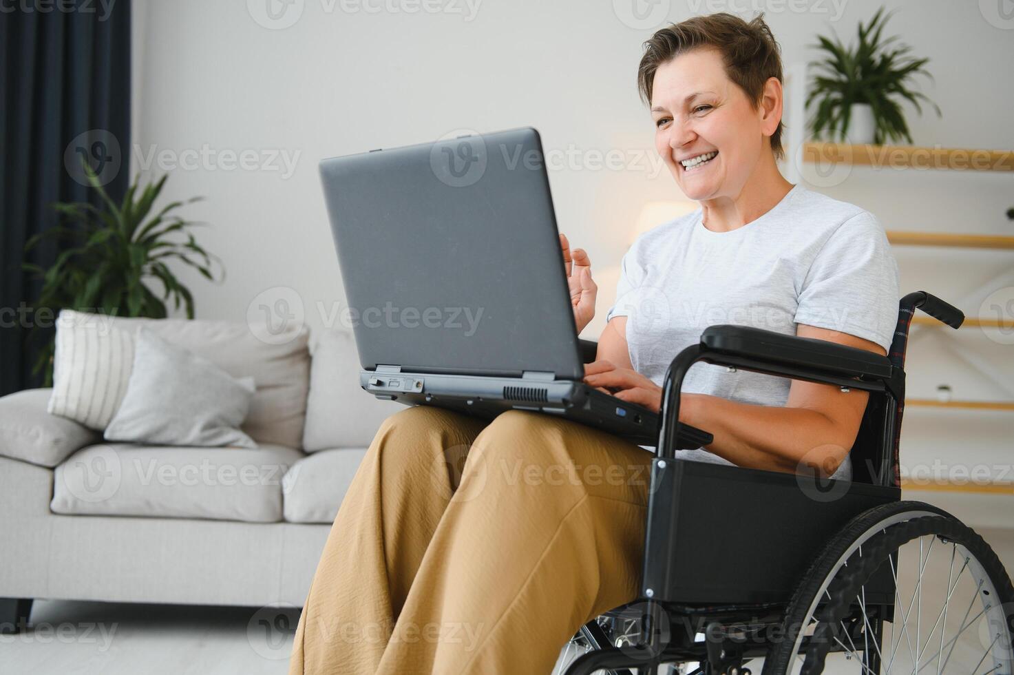 Positive elderly woman in wheelchair working on laptop, IT freelancer, online photo