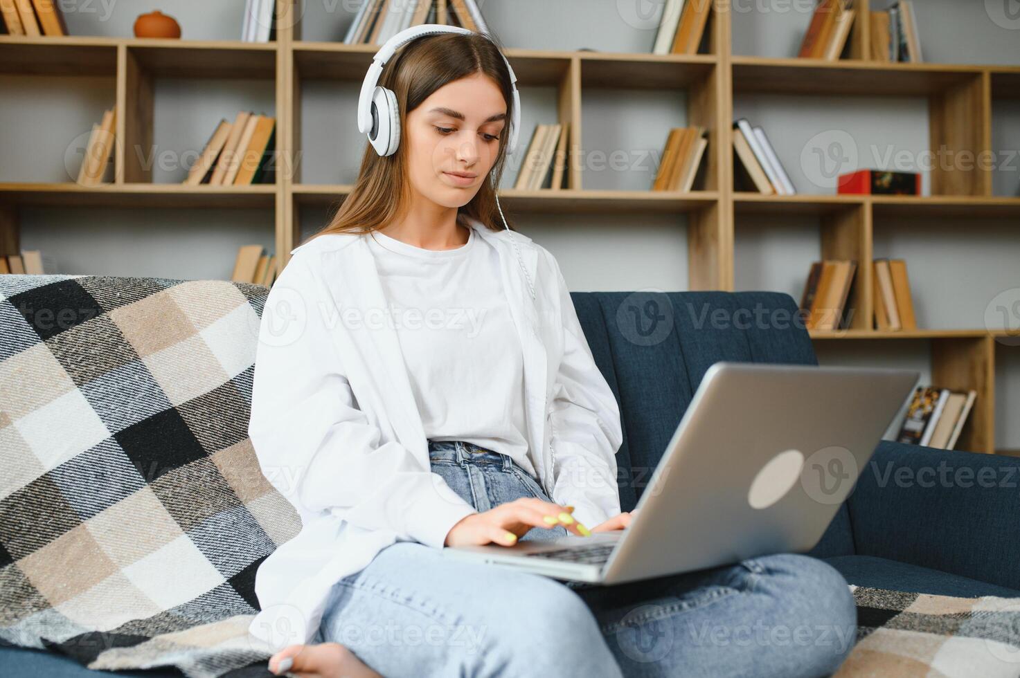 Smiling attractive young woman sitting on sofa using laptop communicating working online at home, happy teen girl typing on computer, enjoying writing blog or chatting with friends in social network photo