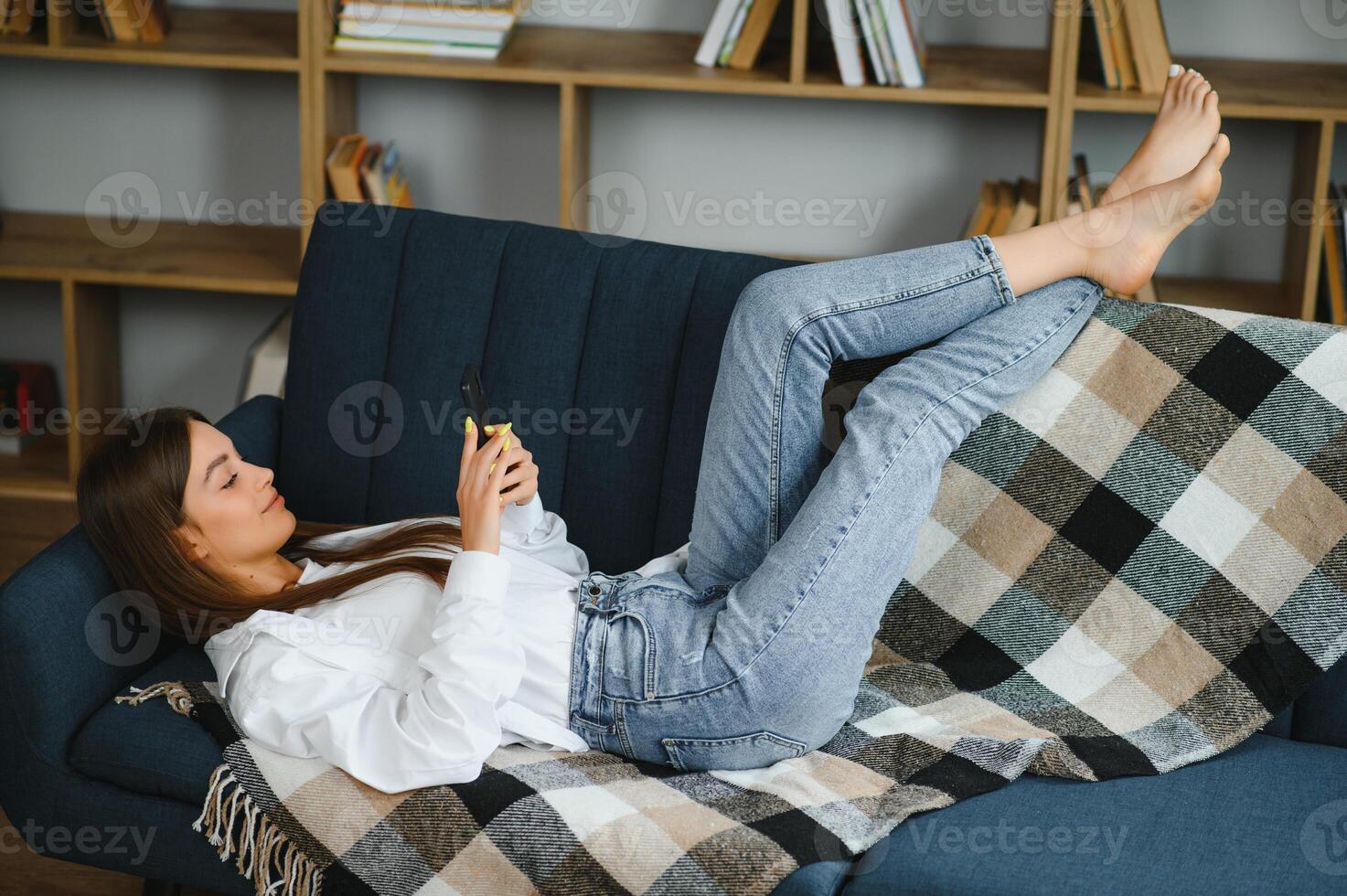 Close up of a relaxed girl using a smart phone lying on a sofa in the living room at home. photo