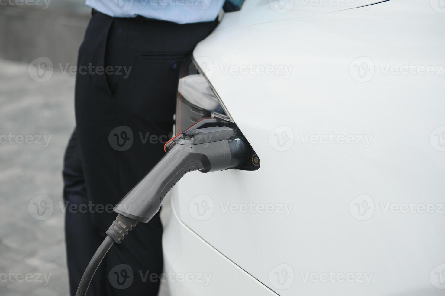 Casual man with smartphone near electric car waiting for the finish of the battery charging process photo