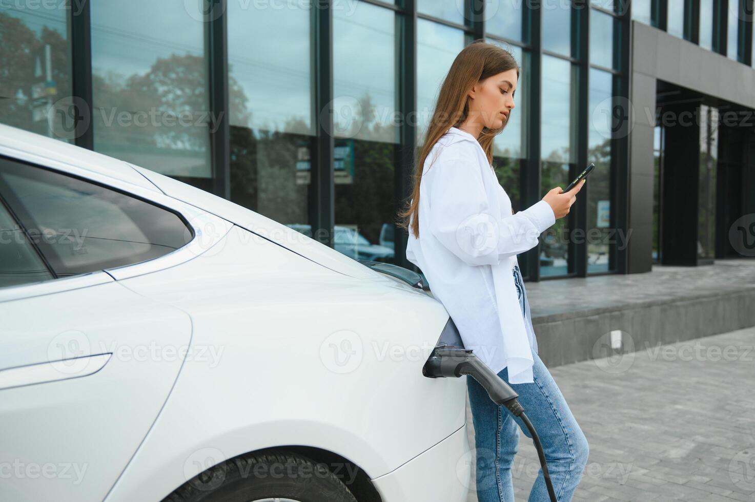 Woman near electric car. Vehicle charged at the charging station. photo