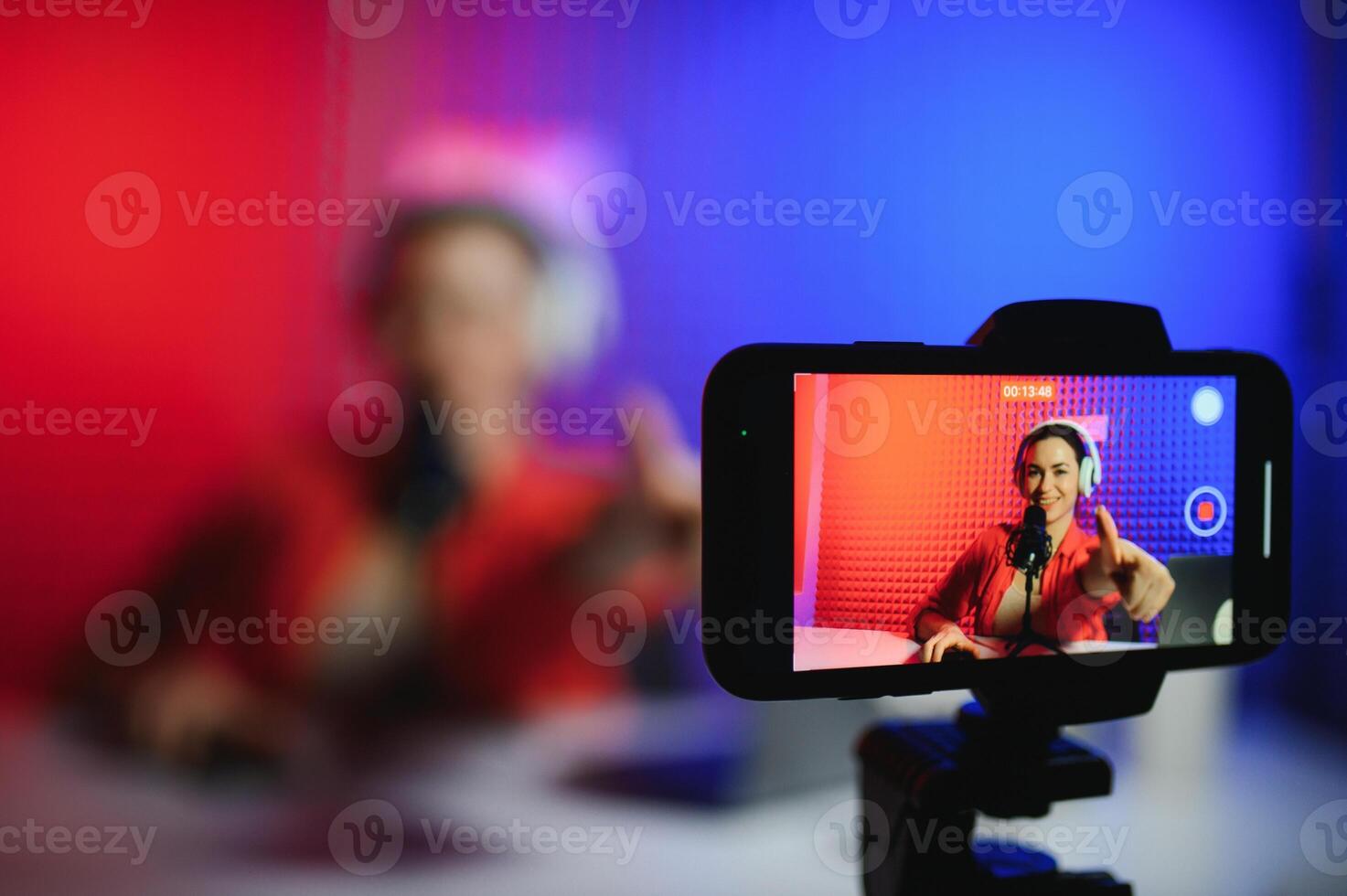 Positive trendy blogger woman speaking at smartphone webcam on tripod, recording post for vlog photo