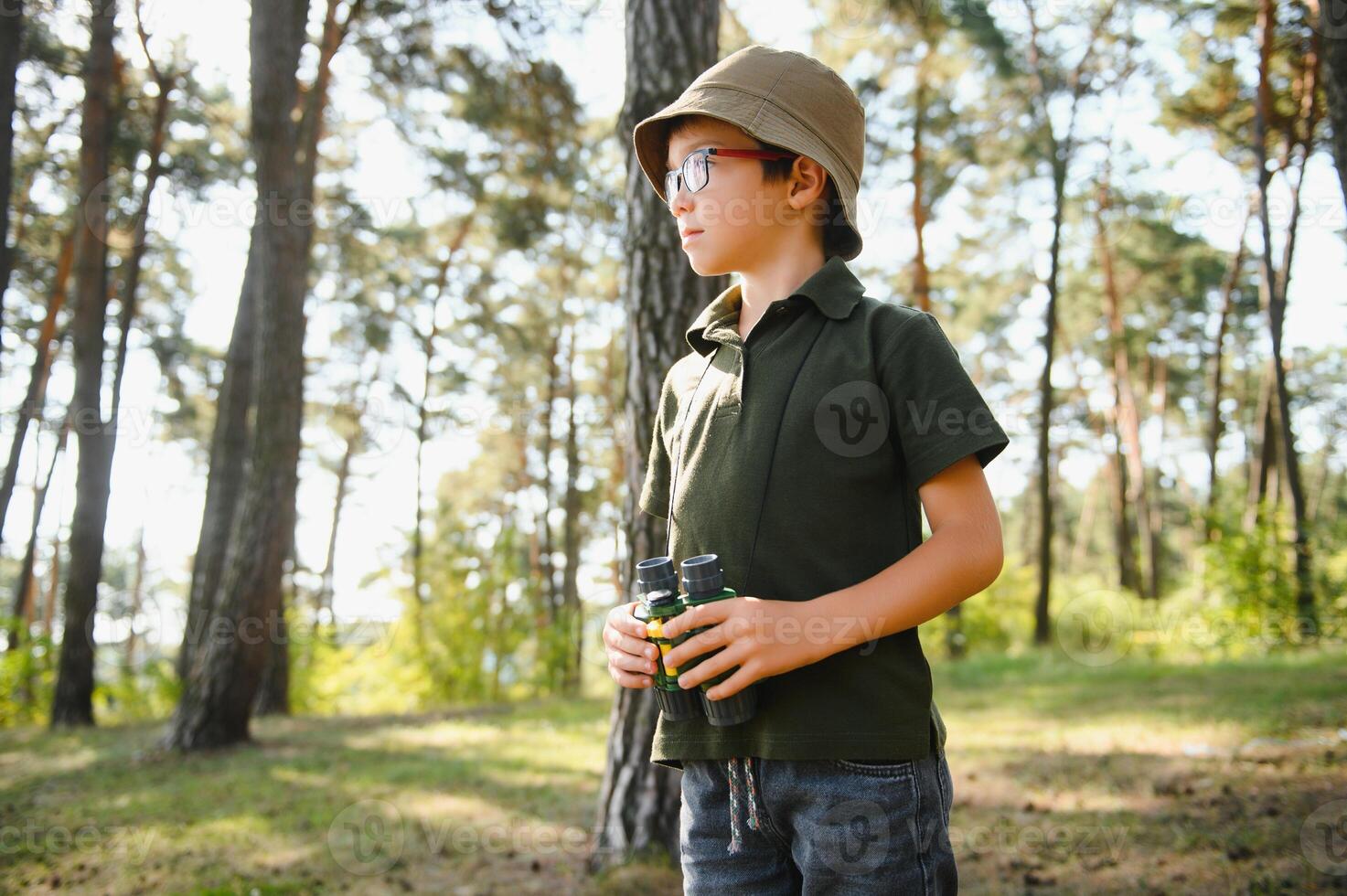 Boy with binoculars. Kid in green forest at summer daytime together. photo
