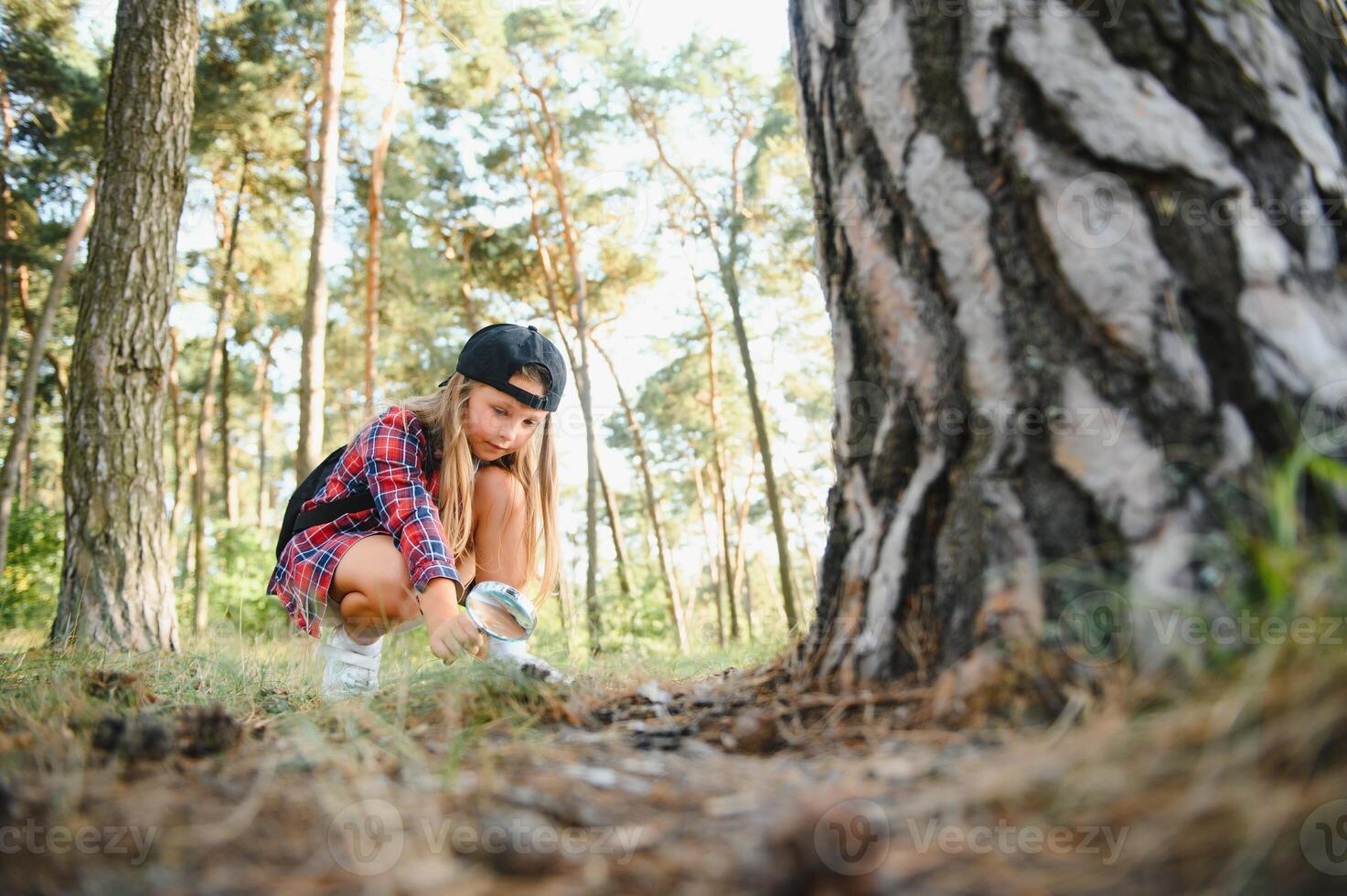 Image of cute kid with magnifying glass exploring the nature outdoors. Adorable little girl playing in the forest with magnifying glass. Curious child looking through magnifier on a sunny day in park. photo