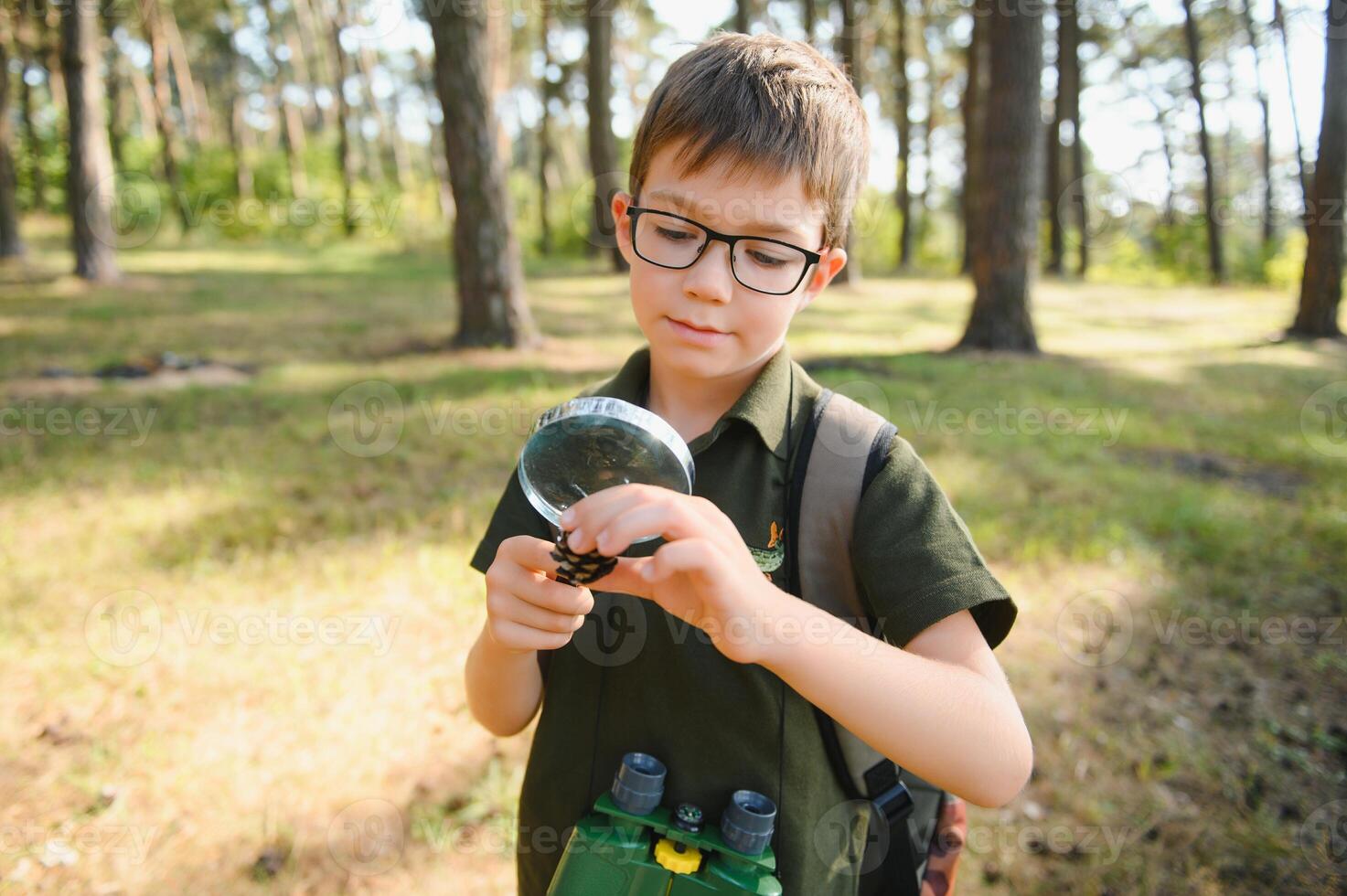 schoolboy is exploring nature with magnifying glass. Summer vacation for inquisitive kids in forest. Hiking. Boy-scout. photo