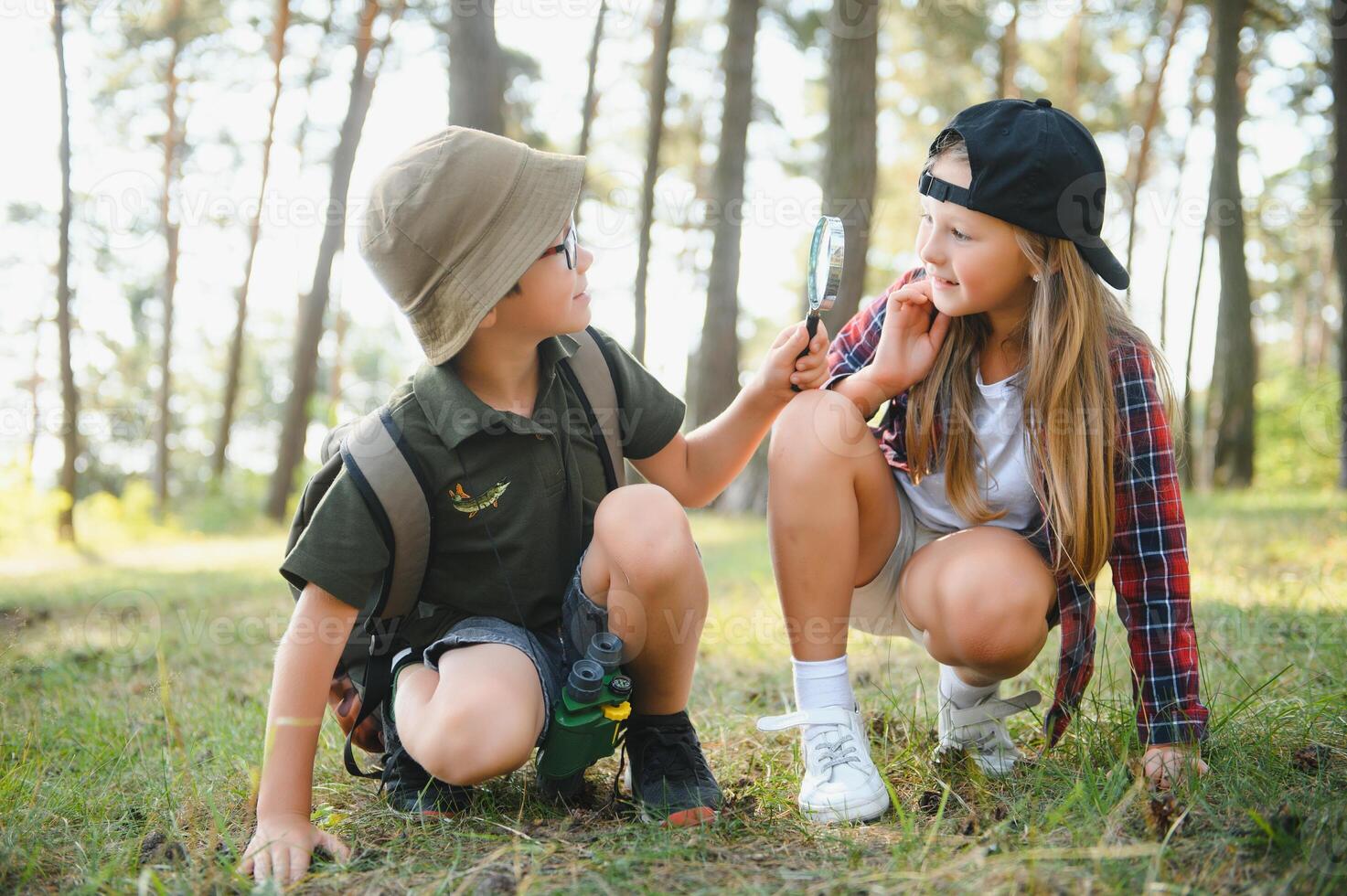Two happy children having fun during forest hike on beautiful day in pine forest. Cute boy scout with binoculars during hiking in summer forest. Concepts of adventure, scouting and hiking tourism photo