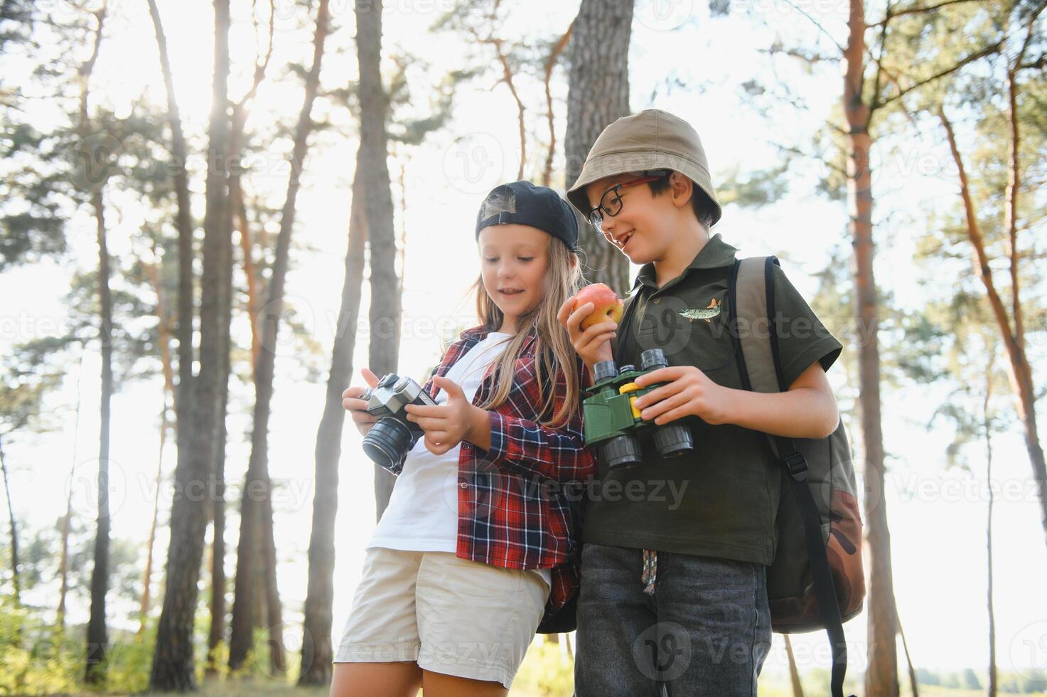 Happy excited school children with backpacks in casual clothes enjoying walk in forest on sunny autumn day, two active kids boy and girl running and playing together during camping trip in nature. photo