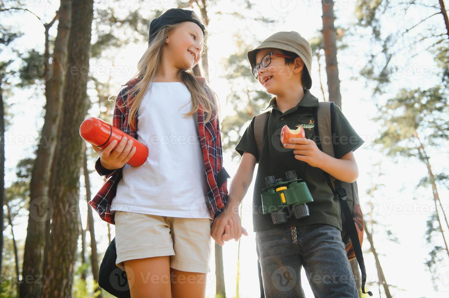 Happy excited school children with backpacks in casual clothes enjoying walk in forest on sunny autumn day, two active kids boy and girl running and playing together during camping trip in nature. photo