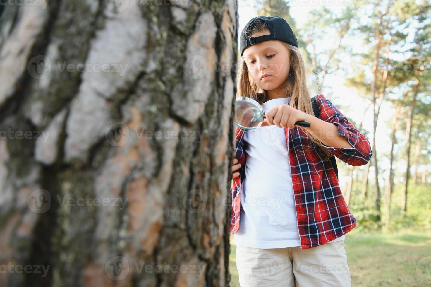 Image of cute kid with magnifying glass exploring the nature outdoors. Adorable little girl playing in the forest with magnifying glass. Curious child looking through magnifier on a sunny day in park. photo