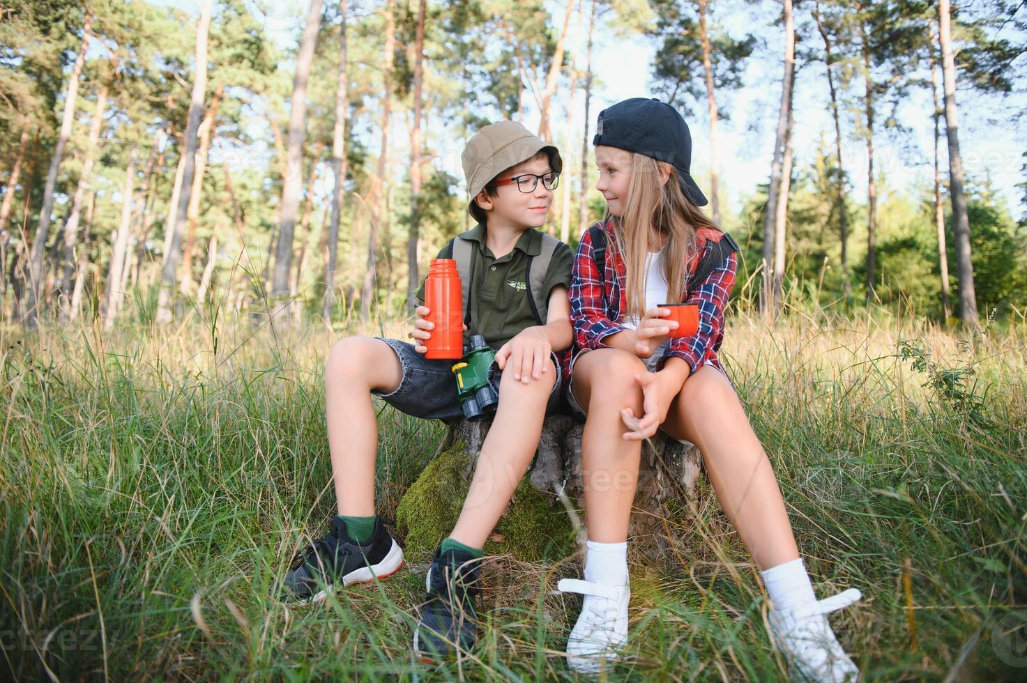 Girl and boy scout sitting and drinking hot tea from thermos in the woods photo