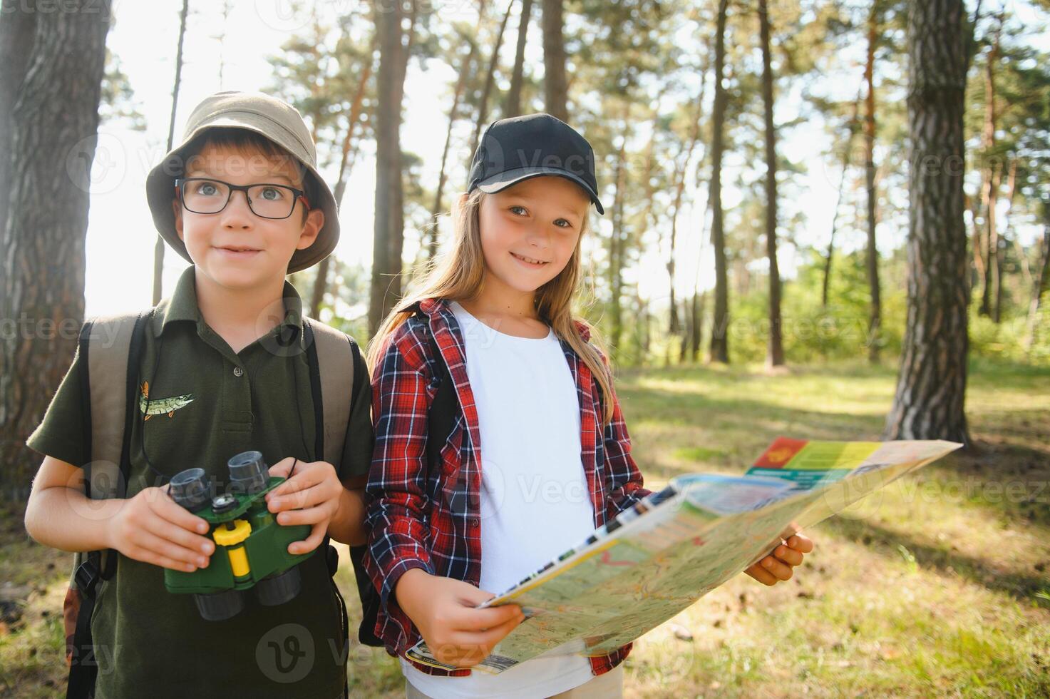 Two happy children having fun during forest hike on beautiful day in pine forest. Cute boy scout with binoculars during hiking in summer forest. Concepts of adventure, scouting and hiking tourism photo