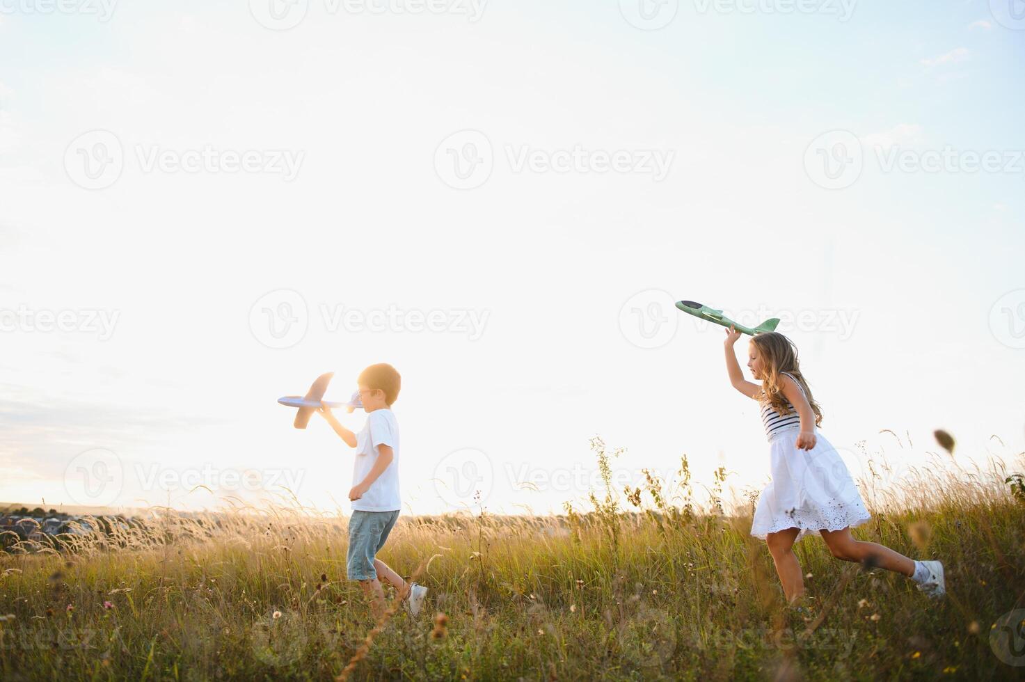 Running boy and girl holding two green and blue airplanes toy in the field during summer sunny day photo