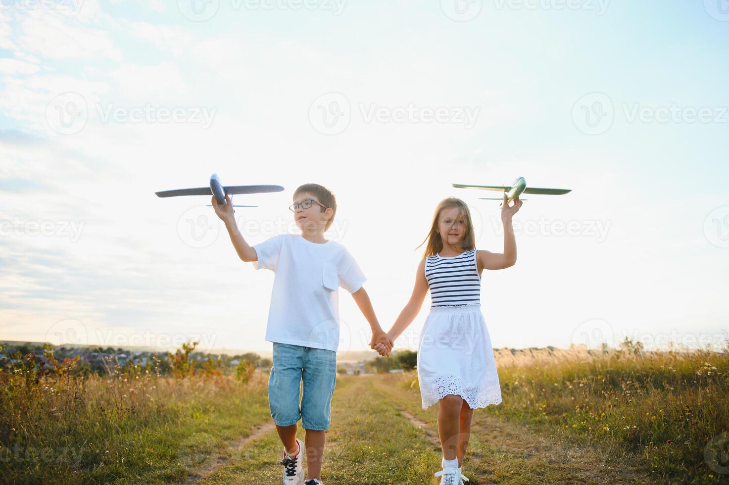 Running boy and girl holding two green and blue airplanes toy in the field during summer sunny day photo