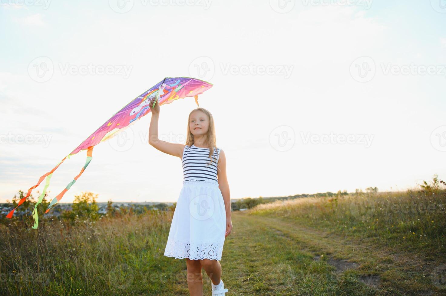 Little cute 7 years old girl running in the field with kite on summer day photo