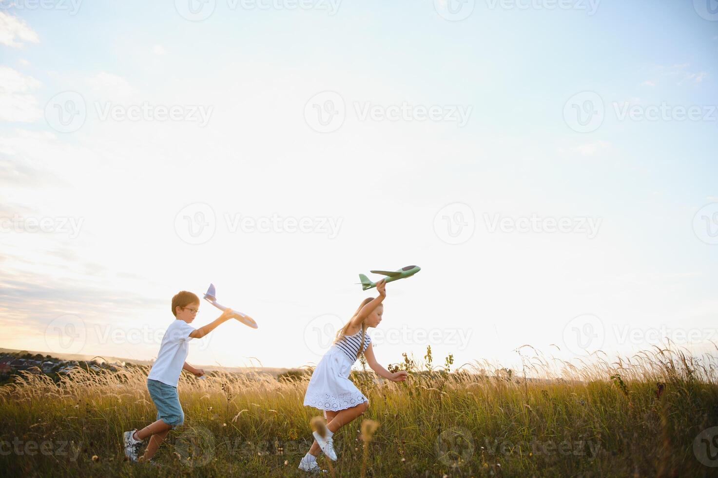 Running boy and girl holding two green and blue airplanes toy in the field during summer sunny day photo