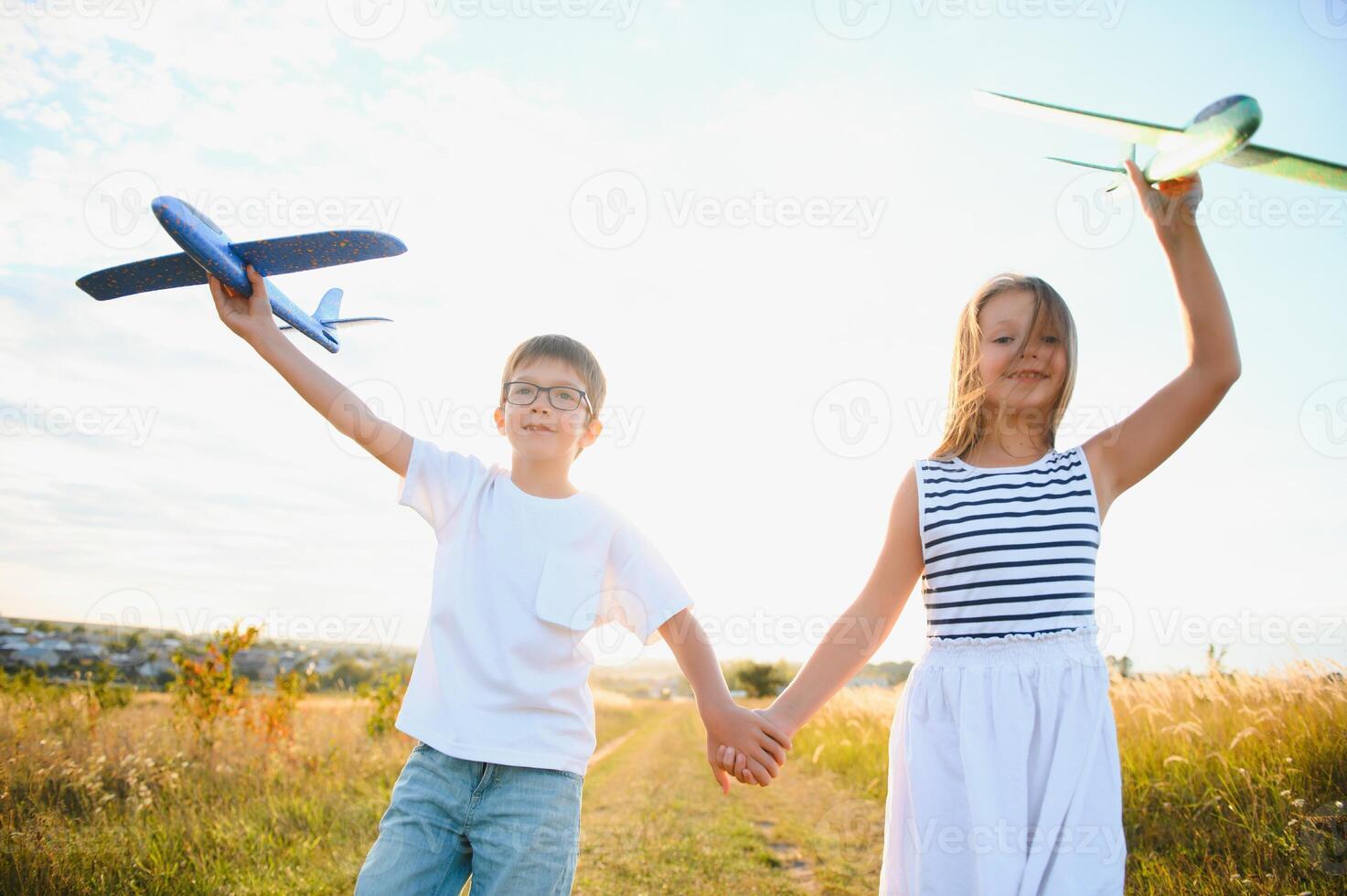 Running boy and girl holding two green and blue airplanes toy in the field during summer sunny day photo