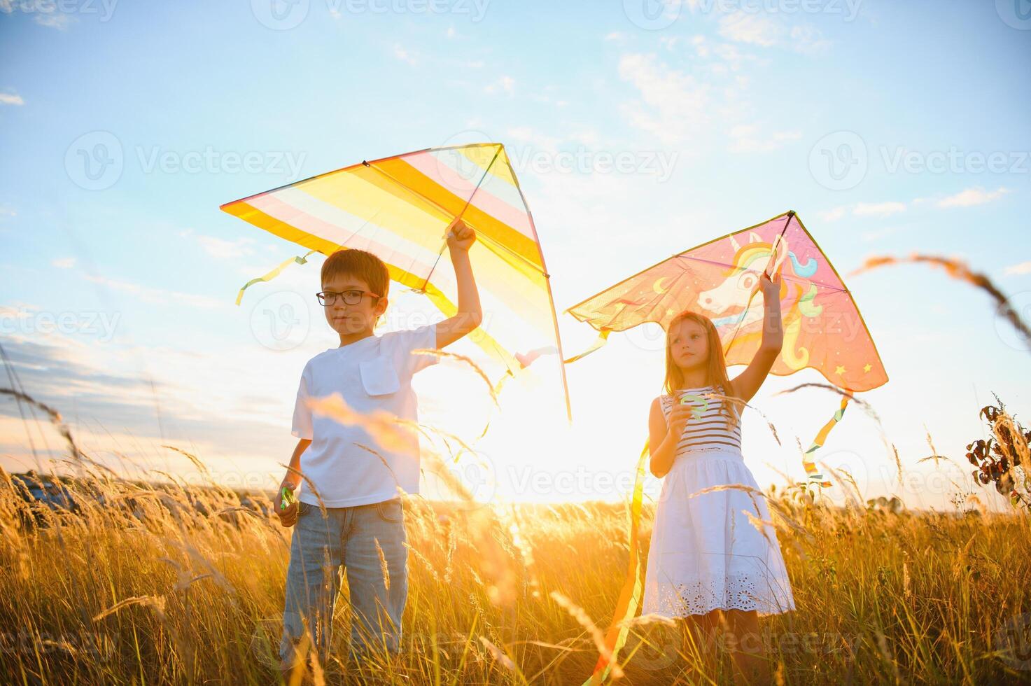 Happy boy and girl playing with kites in field at sunset. Happy childhood concept. photo