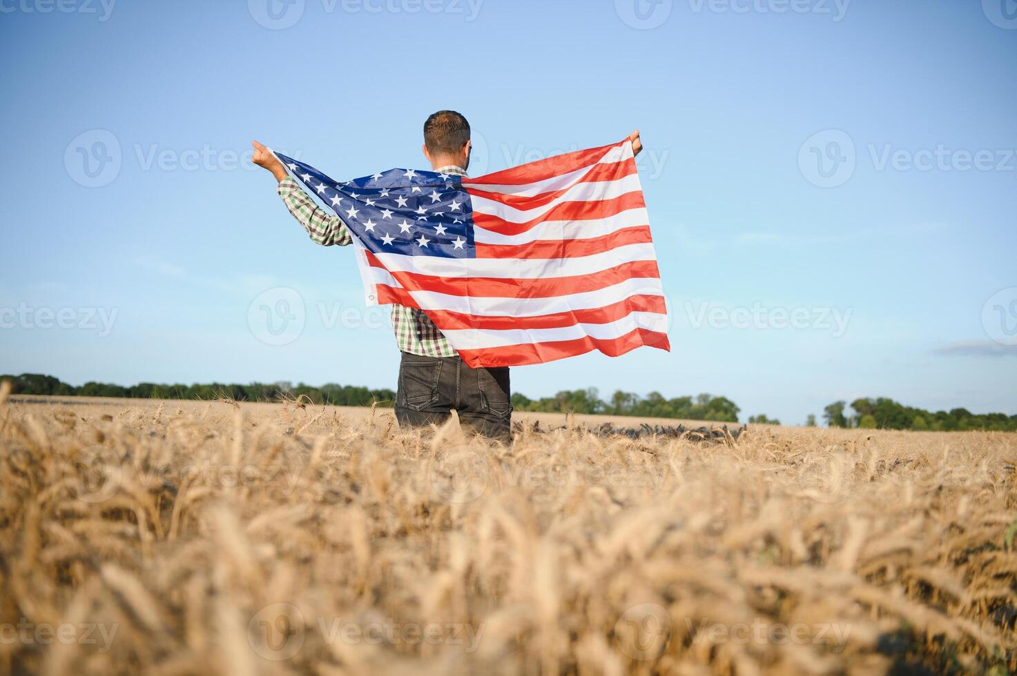 Young man holding American flag, standing in wheat field photo