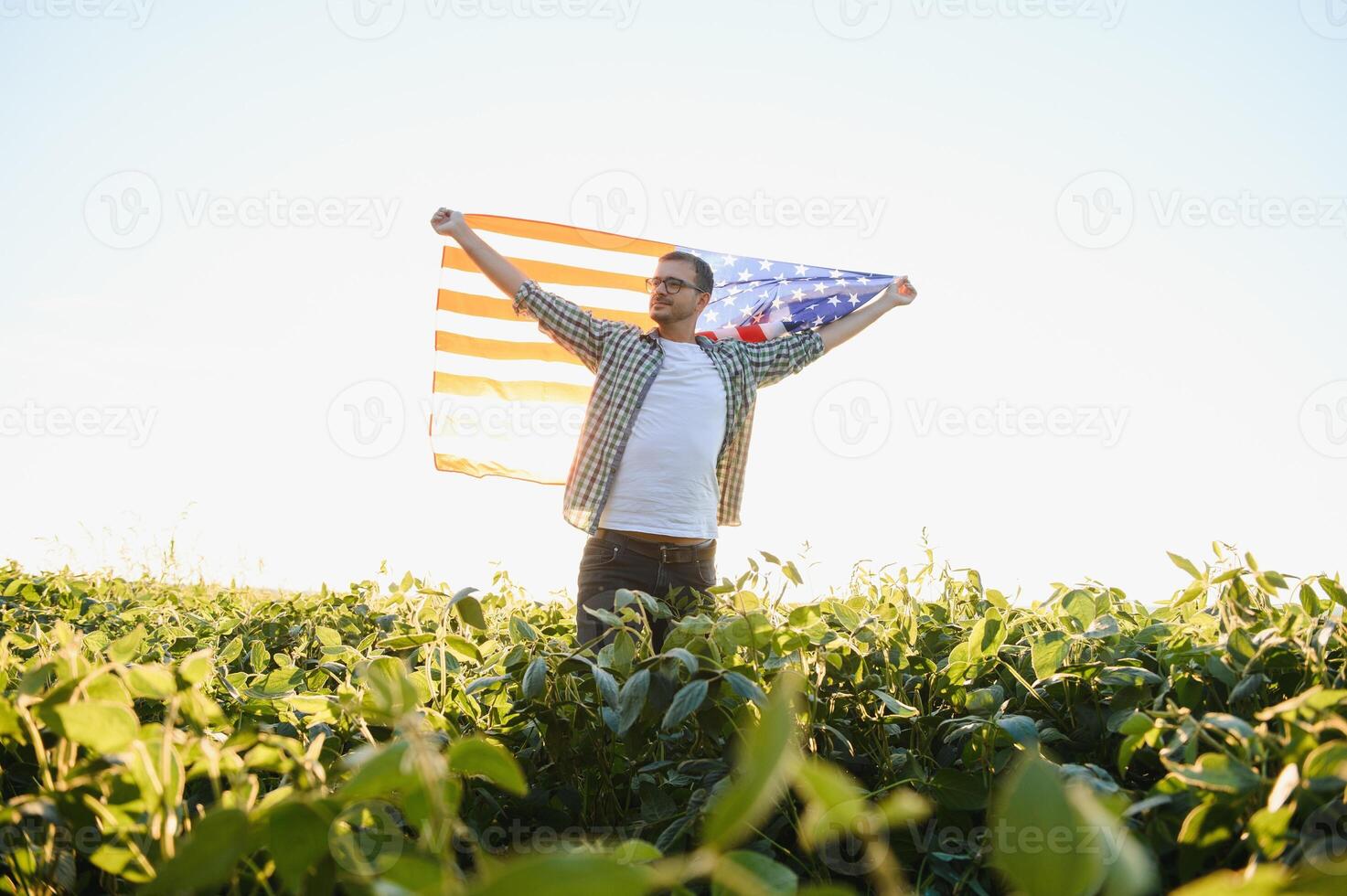 A young farmer stands with a USA flag in a soybean field. The concept of the US agricultural industry. photo