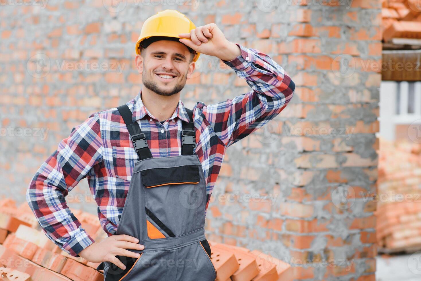 Construction worker man in work clothes and a construction helmet. Portrait of positive male builder in hardhat working at construction site. photo
