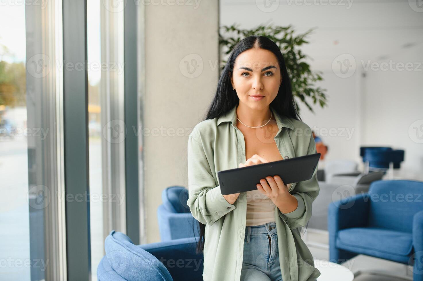 Young modern female freelancer in airport lounge or business center and works using digital tablet, creating new design project photo