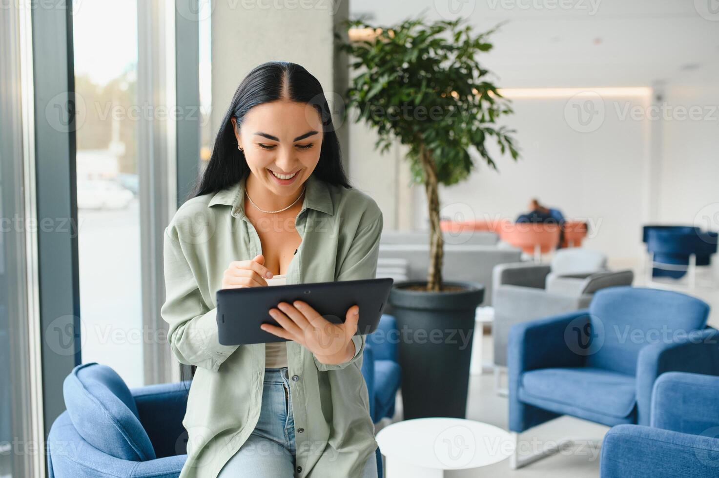 Young modern female freelancer in airport lounge or business center and works using digital tablet, creating new design project photo