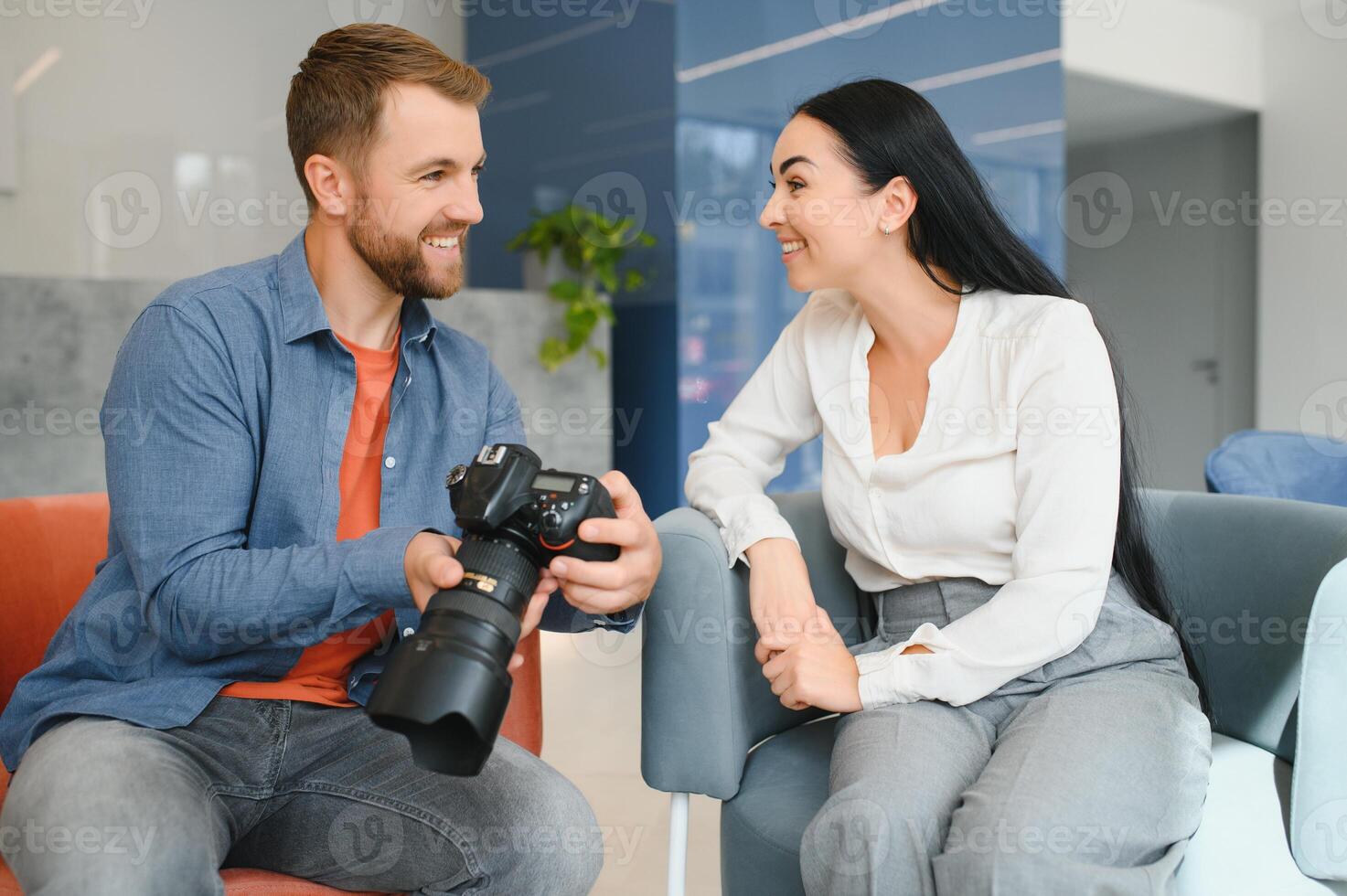 Photographer in office shows photo model in camera. Consultant adjusts activities company as whole. Photo session employees in workplace. Manager well-executed project. Photos best employees company.