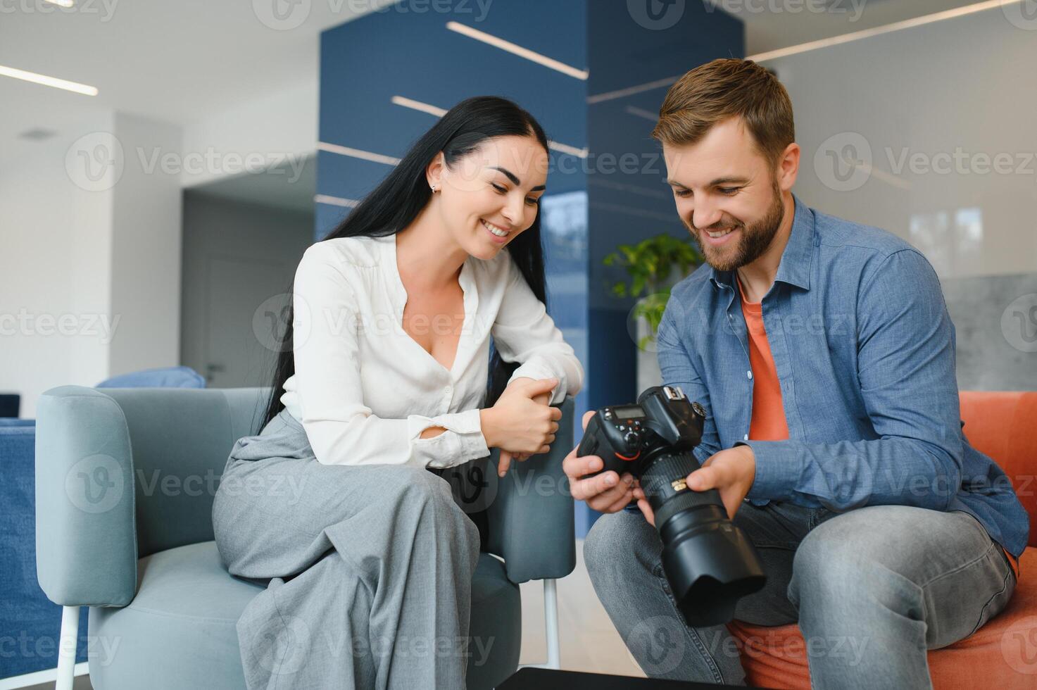 Photographer in office shows photo model in camera. Consultant adjusts activities company as whole. Photo session employees in workplace. Manager well-executed project. Photos best employees company.