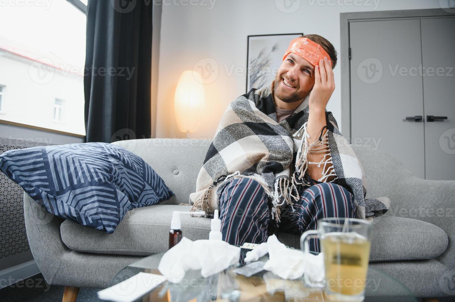 Young man suffering from cold at his home. Shot of a young man sitting on his bed while feeling unwell at home. Trying to stay warm. Sick man photo