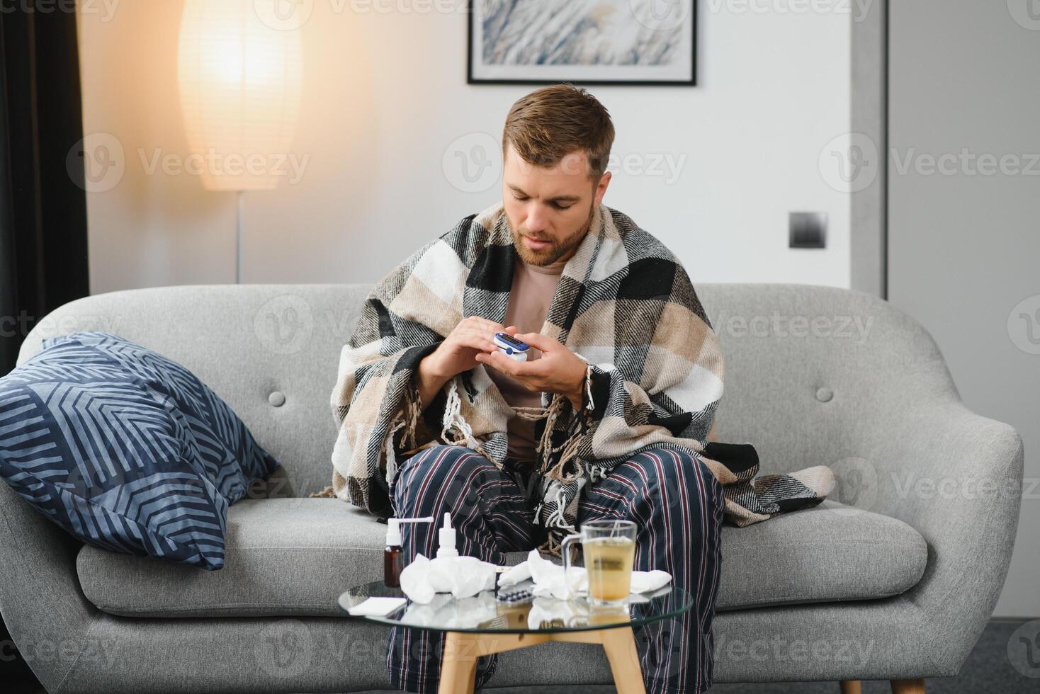 A sick man sits at home on a gray sofa with a blanket. Illness, protection, coronavirus, illness, flu photo