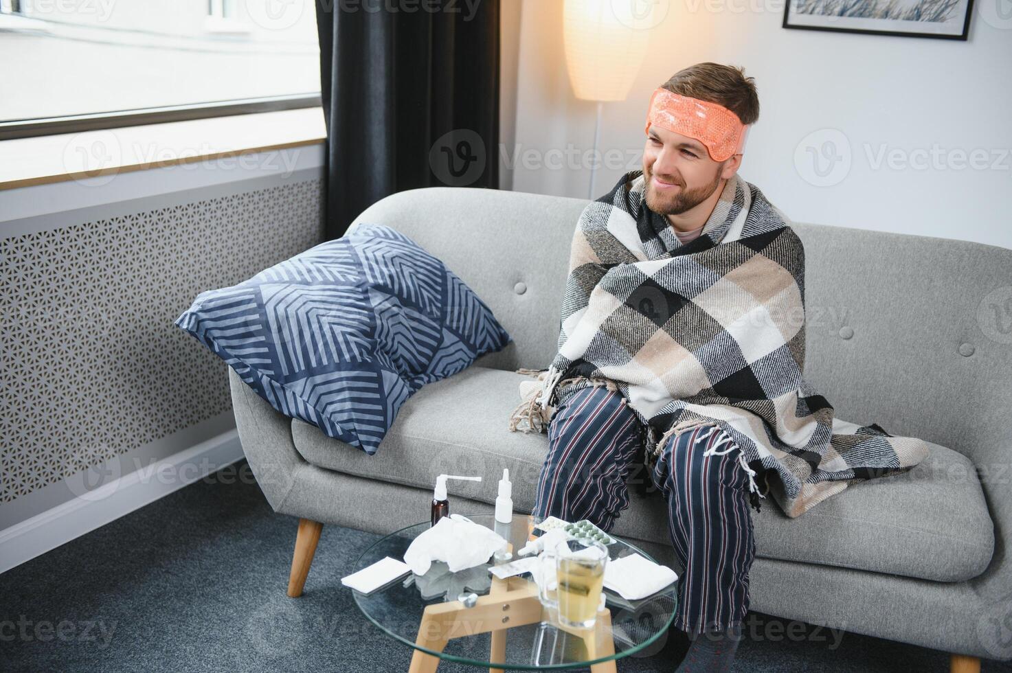 A sick man sits at home on a gray sofa with a blanket. Illness, protection, coronavirus, illness, flu photo