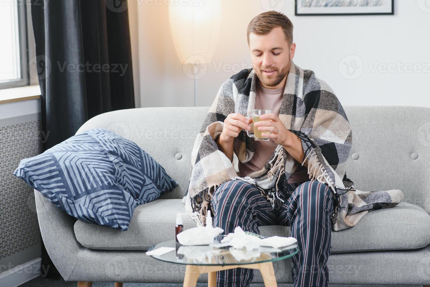 A sick man sits at home on a gray sofa with a blanket. Illness, protection, coronavirus, illness, flu photo