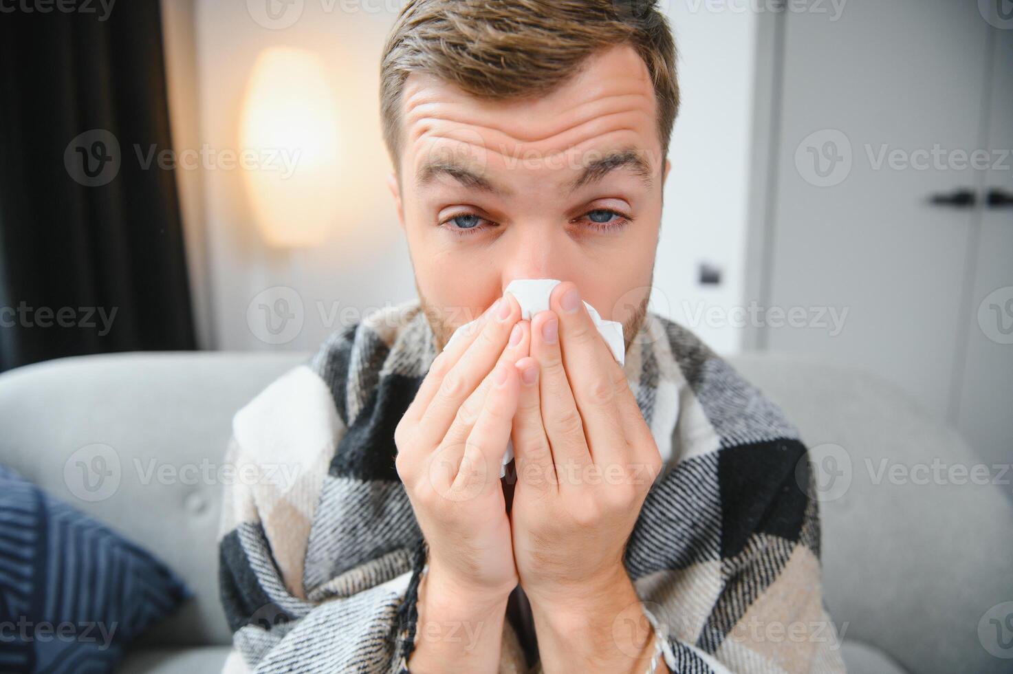 Sick man on sofa at home and blowing nose photo