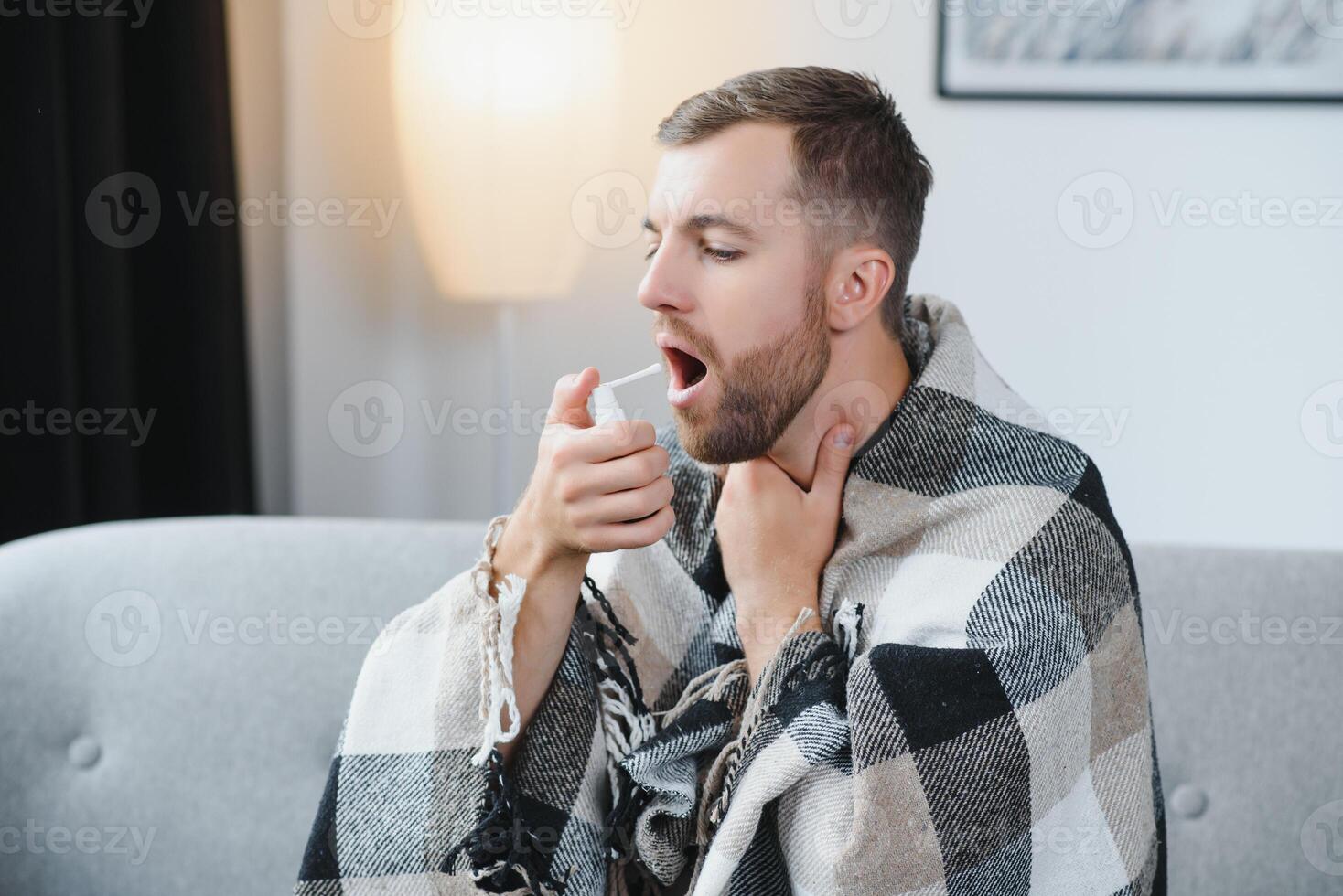 people and health problem concept - unhappy sick man spraying his throat with oral spray in bed at home. photo