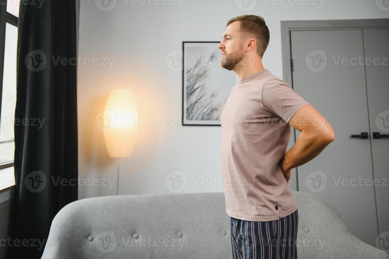 Handsome young man suffering from backache at home. photo