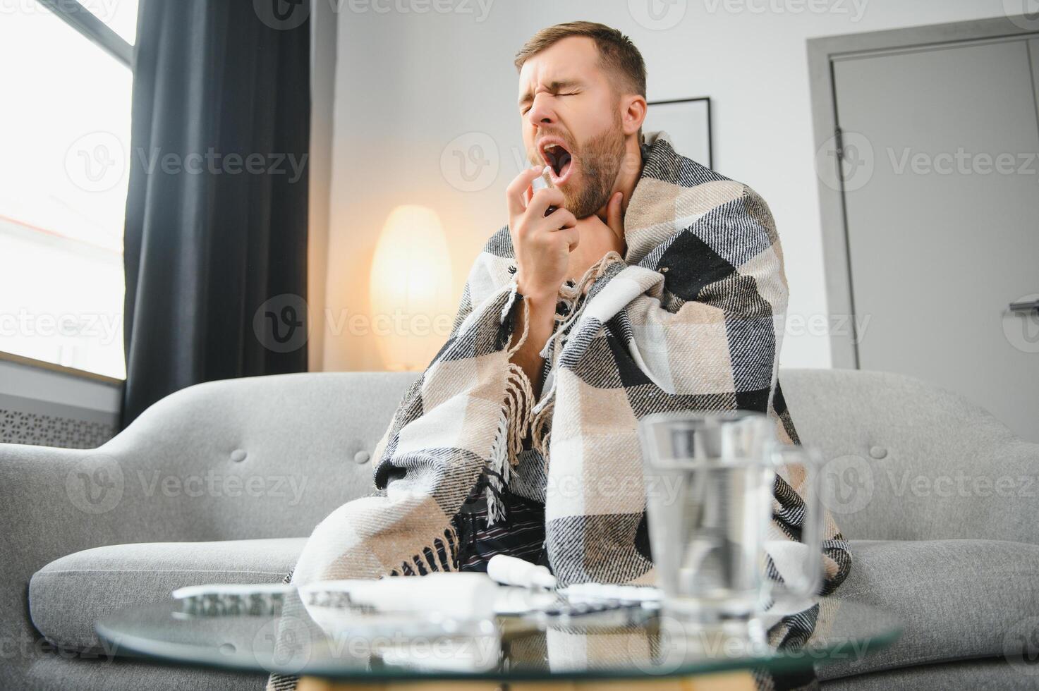 people and health problem concept - unhappy sick man spraying his throat with oral spray in bed at home. photo