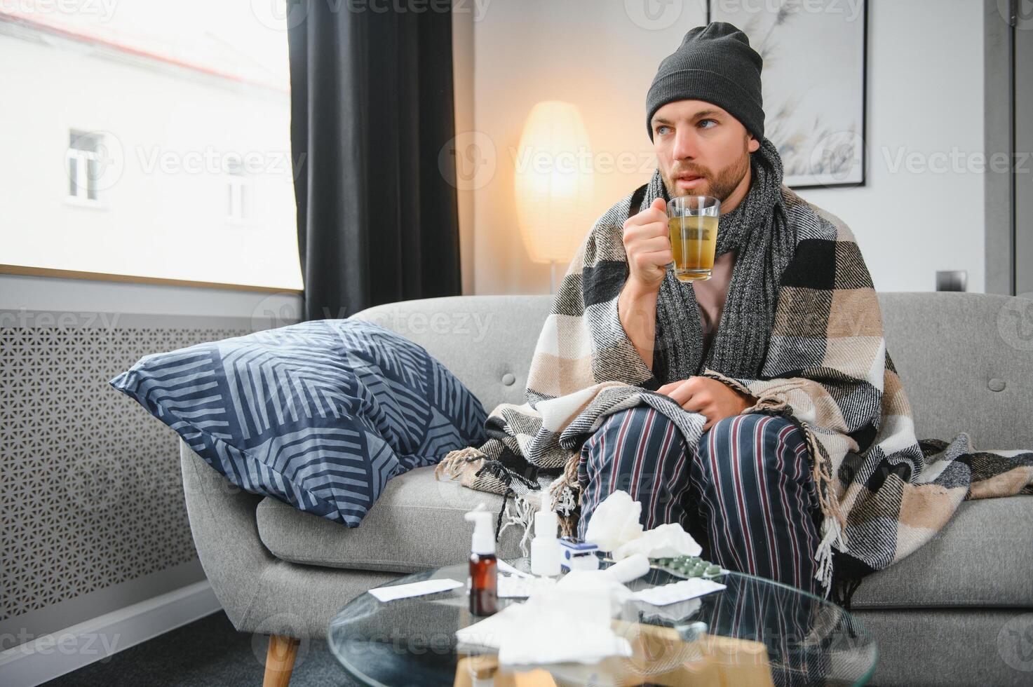 A sick man sits at home on a gray sofa with a white blanket. Illness, protection, coronavirus, illness, flu photo