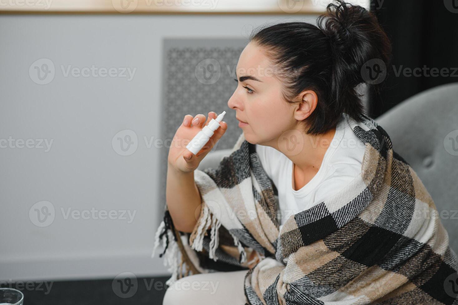 Nasal spray in hand of sick young woman sitting on couch. Allergic rhinitis symptoms and treatment photo
