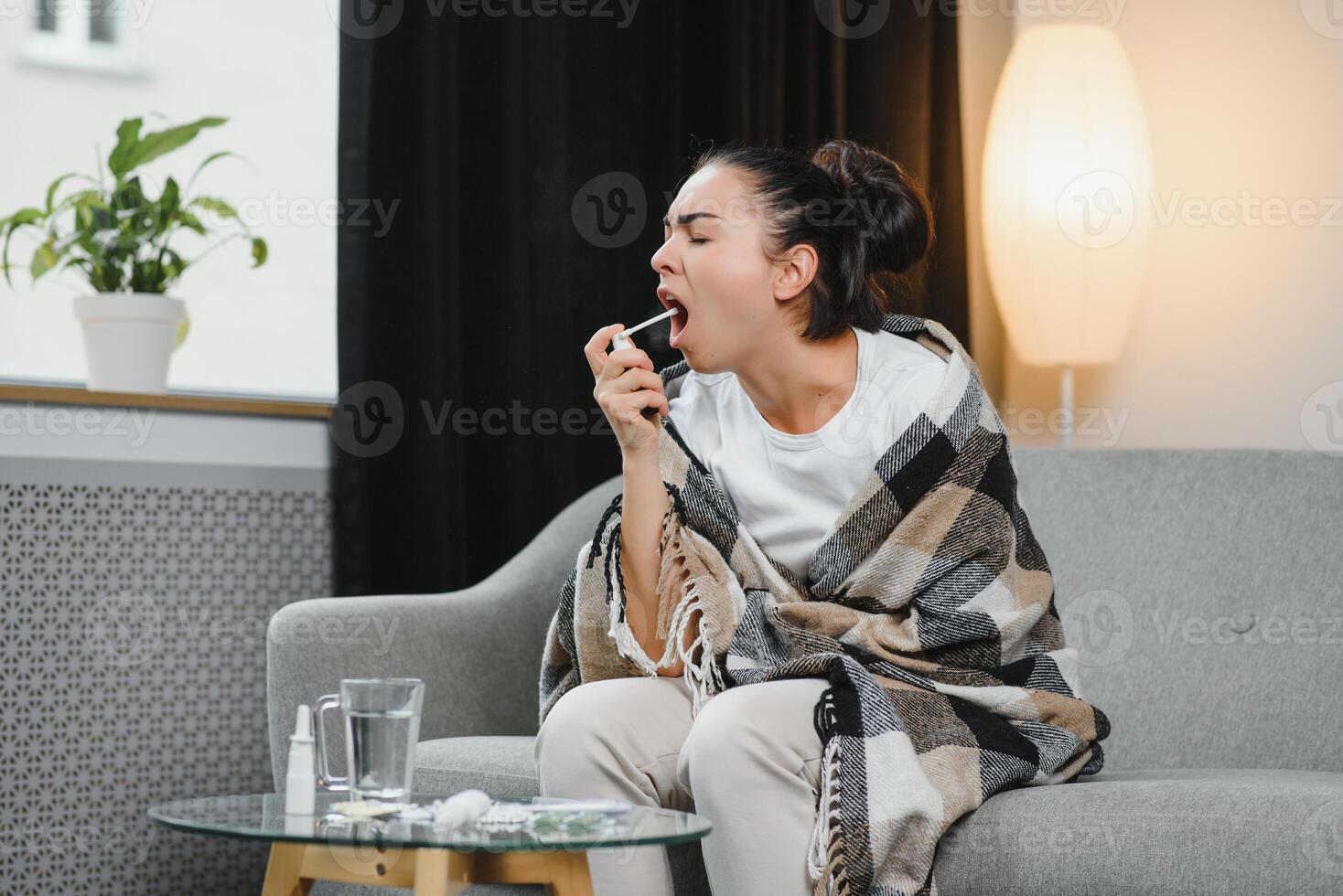 sick young woman in scarf using cough spray. photo