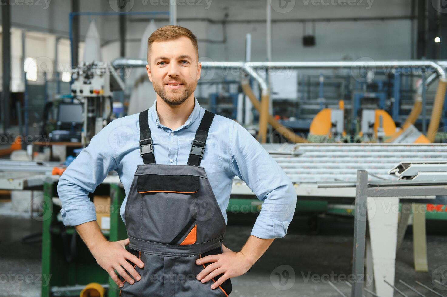 Portrait of factory worker in protective uniform and hardhat standing by industrial machine at production line. People working in industry photo