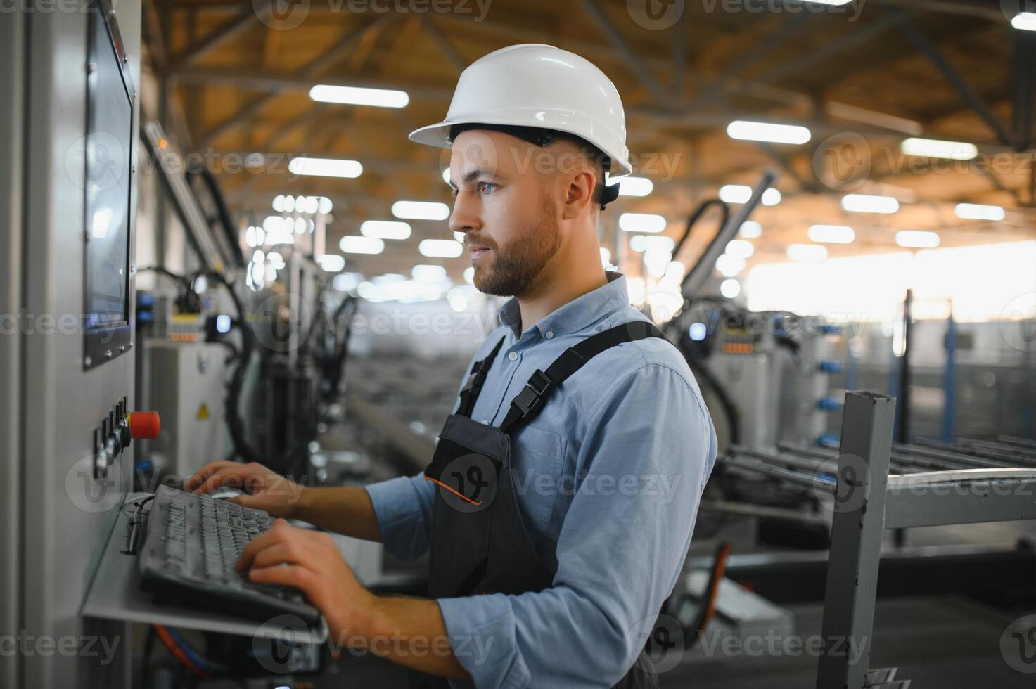 Operator wearing safety hat behind control panel on a factory photo