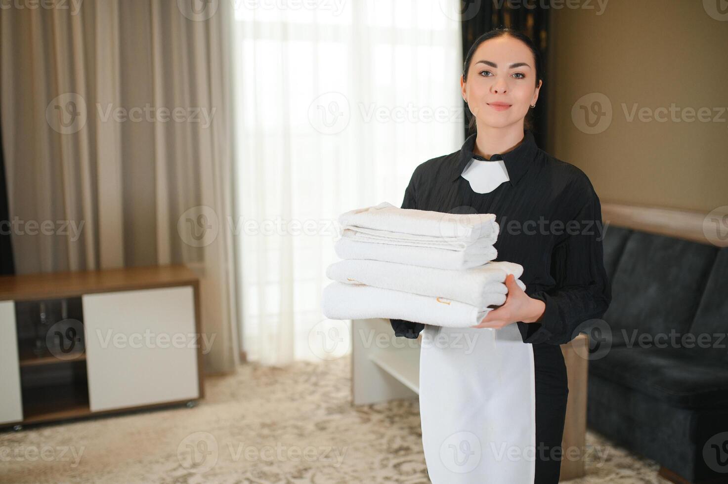 Maid holding fresh towels with flowers in hotel room photo